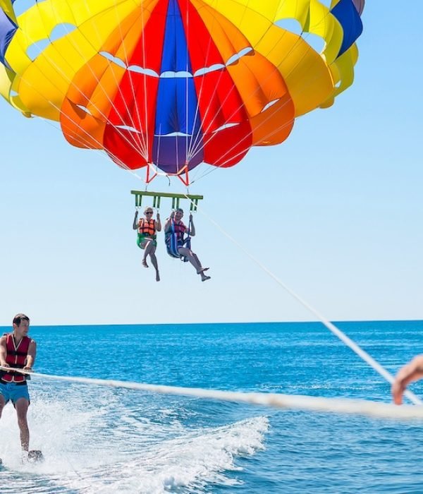 Happy couple Parasailing in Dubai beach in summer. Three people rest on the sea. Parachute and water skiing.